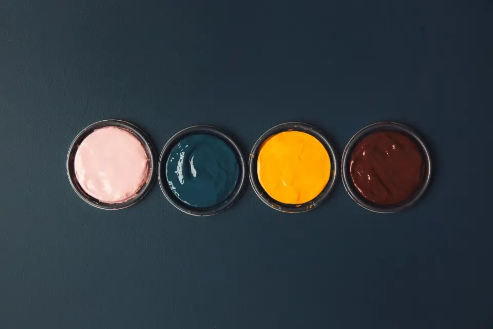 Four open pots of paint in pink, teal, yellow and brown on a dark surface