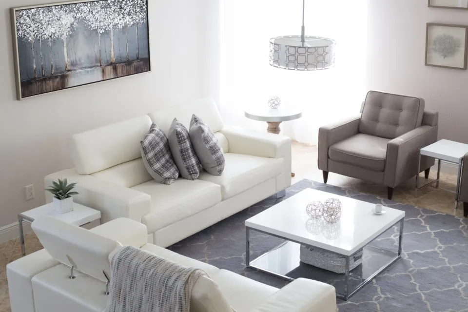 A bright living room with white walls, white sofas and a grey armchair